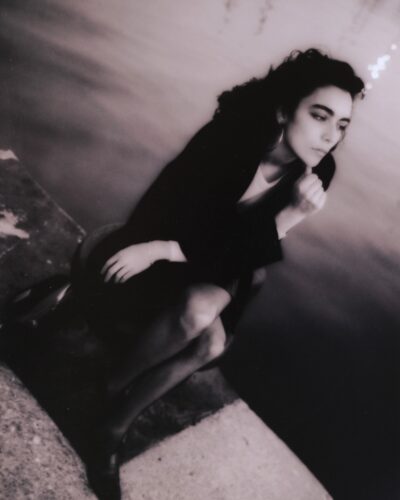 Analogue film photographt of a young woman posing in a dark coat, high contrast cinematic black and white fashion portraiture, Barcelona, Spain, by Jeroen Busschers.