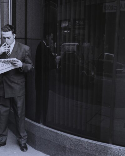Analogue film photography of a buisenessman lighting a cigarette and reading a newspaper with the headline KILLER, cinamatic street photography in London City with window reflections, by Jeroen Busschers